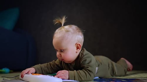 Cute smiling baby lies on the floor on his belly. Infant plays with a toy and looks up laughing.
