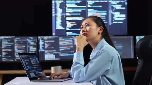 Vue latérale d'une programmeuse asiatique pensant à quelque chose tout en écrivant du code sur un ordinateur portable