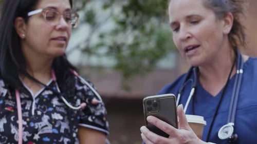 Cheerful nurses using phone on bench in Canada during the coronavirus pandemic