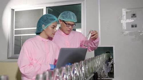 Deux ingénieurs supervisent le contrôle qualité en vérifiant les bouteilles de produits sur le tapis roulant d'une usine de boissons