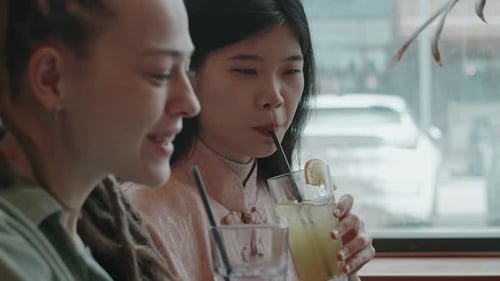 Two Female Friends Sipping Cocktails Talking and Smiling in Restaurant
