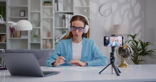 Vloguera de negocios segura de sí misma con auriculares hablando con la cámara filmando un vlog de negocios en vivo c