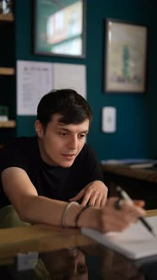 A Young Professional is Focused While Writing Notes at Their Desk in a Modern Office Environment
