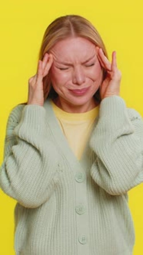 Woman Massaging Temples in Frustration on Yellow Background