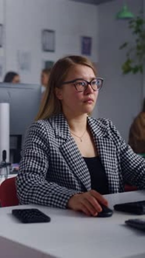 Focused Young Professional in Checkered Blazer Working at Computer in Modern Open Plan Office with