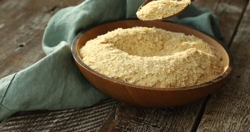 Nutritional Yeast Flakes Being Spooned into a Wooden Bowl