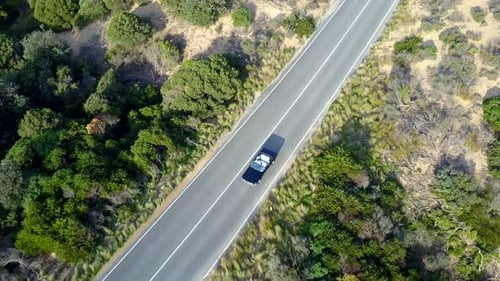 Aerial footage of a black vintage car on the road near a beach.