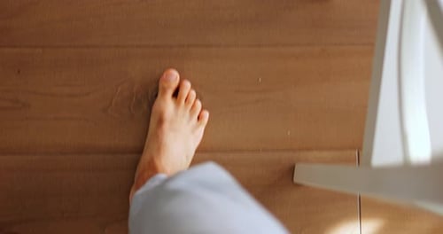 Man with Bare Feet Walks on Wooden Floor of Room with Bright Sun Glare