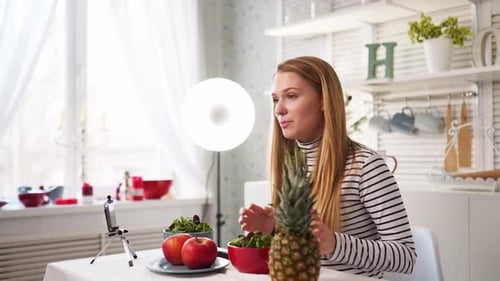 Un bloguero gastronómico cocinando ensalada vegana fresca de frutas en un estudio de cocina, tutorial de filmación ante la cámara para