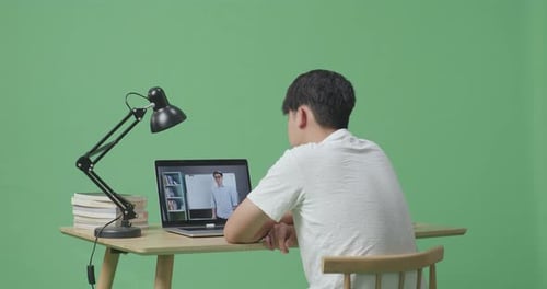 Young Asian Male Looking At A Male Teacher Teaching On A Laptop While Studying On Green Screen
