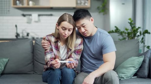 Sad upset couple after negative pregnancy test result. worried young woman and asian man holding