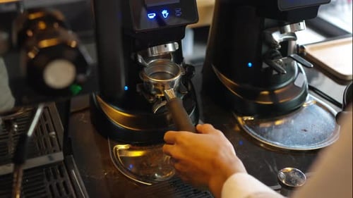 4K Barista grinding roasted coffee beans on grinder machine on counter at cafe.