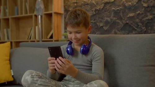 Boy Using Smartphone on Couch with Headphones