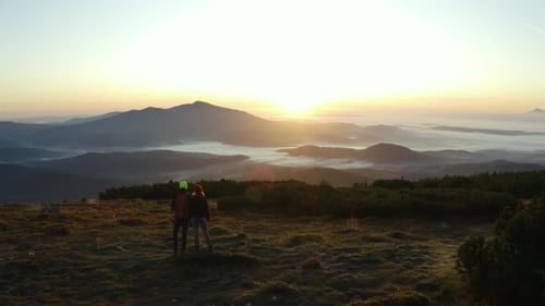 A couple of hikers standing on a rock on top of a mountain during sunrise. Stunning view of dark mou