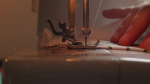 Seitenansicht der Nadel der Nähmaschine in Zeitlupe mit sichtbaren Händen des Bedieners.
