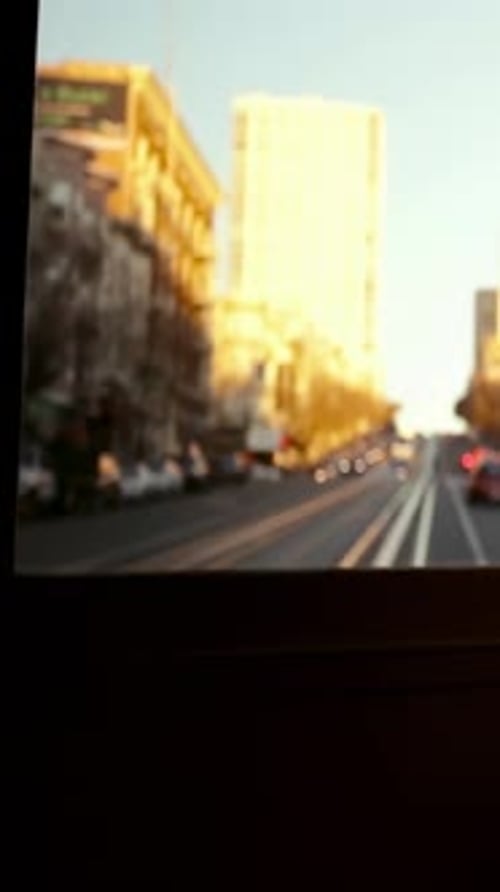 Window framing hill street, vehicle starting uphill, lights glowing, sunlight for urban design