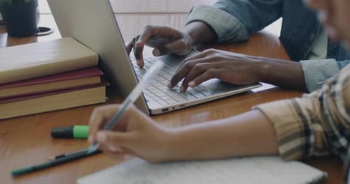Nahaufnahme männlicher und weiblicher Hände beim Schreiben in Notizbuch und Tippen mit Laptop-Computer beim Lernen am