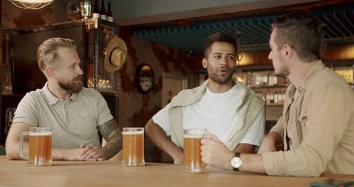 Men friends sitting at table with glass of beer at pub and talking
