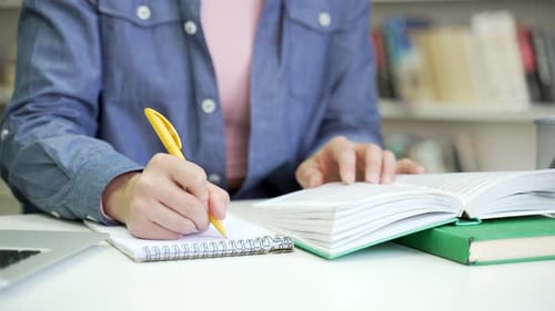 Close up. A female hand writes with a pen in a notebook at the university library. Student reading