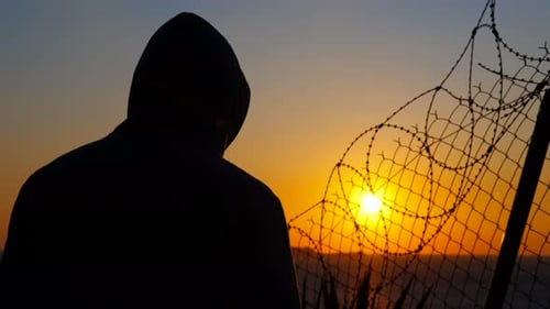 Man Removing Hood at Sunset Behind Barbed Wire Fence