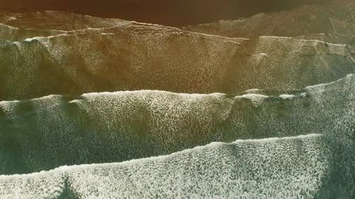 Top view of gentle ocean waves rolling onto sandy beach shoreline