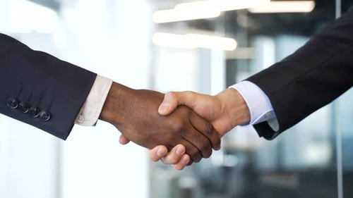 Close-up of two businessmen in formal suits shaking hands against blurred modern office background.