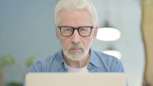 Close Up of Old Man Looking at Camera while using Laptop