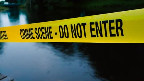 Crime scene police tape ribbon pulled in front of a dark colored summer countryside lake in evening.