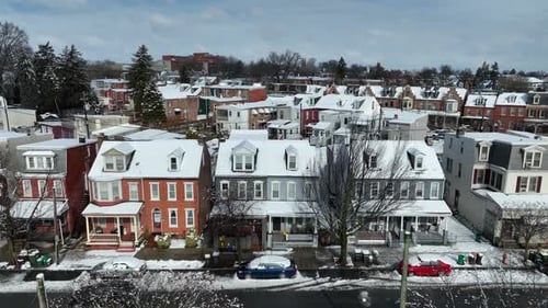 Aerial approaching shot of snowy row of houses and car on street. American neighborhood with snow-co