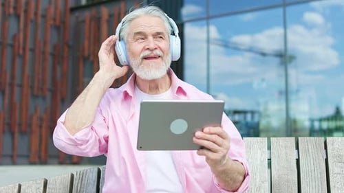 Aged Man in Headphones Using Tablet While Relaxing on Bench