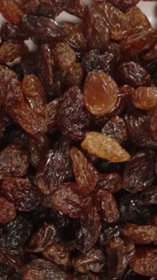 Vertical video. Raisins fall down, top view, in slow motion.