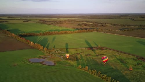 Two Hot Air Balloons are Flying Over Green Fields at Warm Summer Day