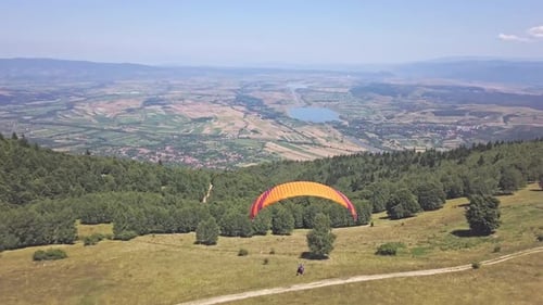 Aerial view from behind the paraglider. Person under large orange parachute flying through the air t
