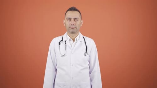 The doctor looks at the camera with a plain expression.