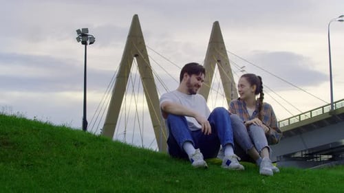 Two Lovers Kissing in the Park on the Grass Against the Backdrop of the Urban Landscape