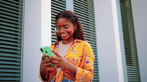 Smiling Woman Uses Phone Outside in Urban Setting