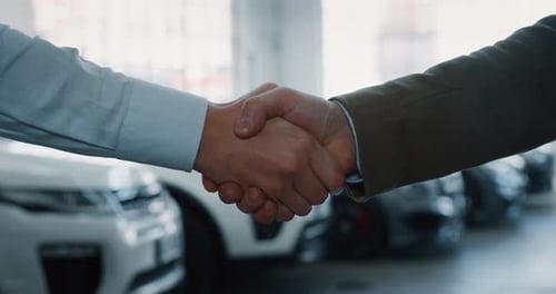 Close up of dealer and new owner handshake after concluding a car deal in auto show or salon. Slow
