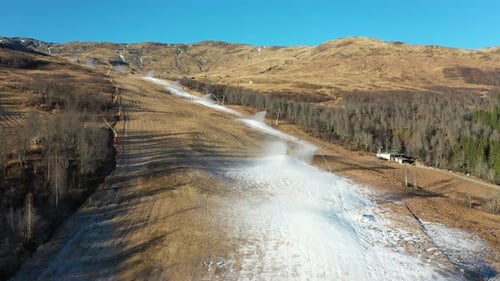 Flyover above artificial snow being sprayed on large ski run slope in Myrkdalen, Norway