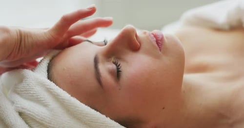 Nahaufnahme zweier junger Freundinnen mit einem Handtuch auf dem Kopf, die eine Gesichtsmassage und einen Wellness-Aufenthalt erhalten