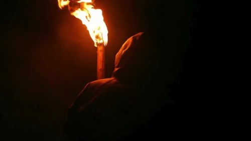Hooded Figure Holding Flaming Torch in the Dark