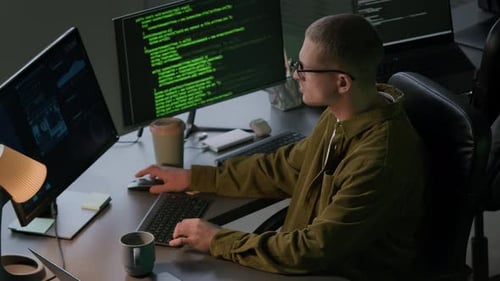 Young Male Programmer Working at Computer Desk in Evening Office