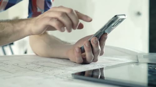 Man Inspecting Blueprints While Using Smart Phone