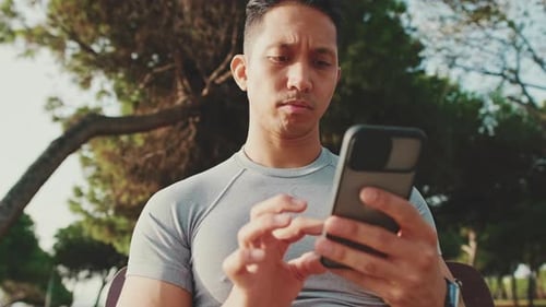 Young man sitting on a park bench uses a mobile phone