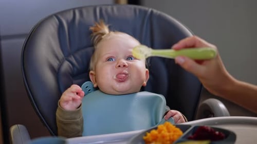Adorable Infant Being Spoon Fed in Highchair