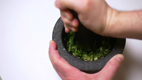 Mit frischem Knoblauch, Koriander, schwarzen Pfefferkörnern und Salz gefüllter Mörser und Stößel in Zeitlupe