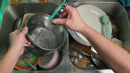 Man Washes a Dirty Pan at Home in the Kitchen