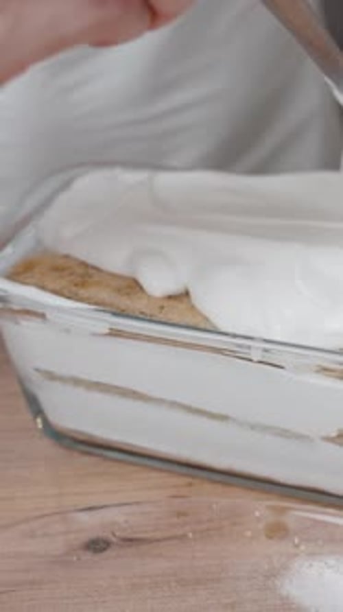 Vidéo verticale. La femme prépare le tiramisu, elle étale uniformément la couche supérieure de crème
.