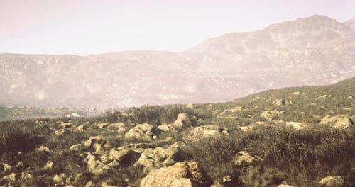 Rocky Landscape with Distant Mountains Under a Hazy Sky During Warm Daylight