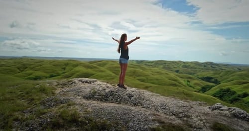 Junge Frau mit offenen Armen feiert Freiheit auf dem Gipfel der grünen Hügel auf Sumba Island