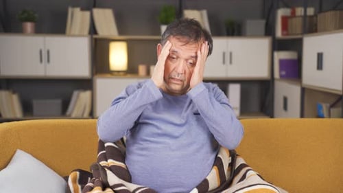Man Rubbing Head on Couch Feeling Ill